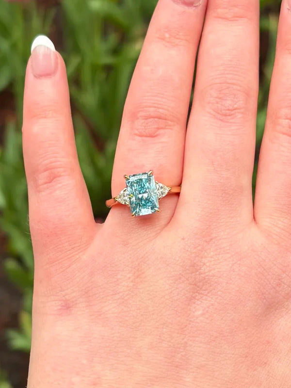 Ring with a blue gemstone on a hand against a blurred green background