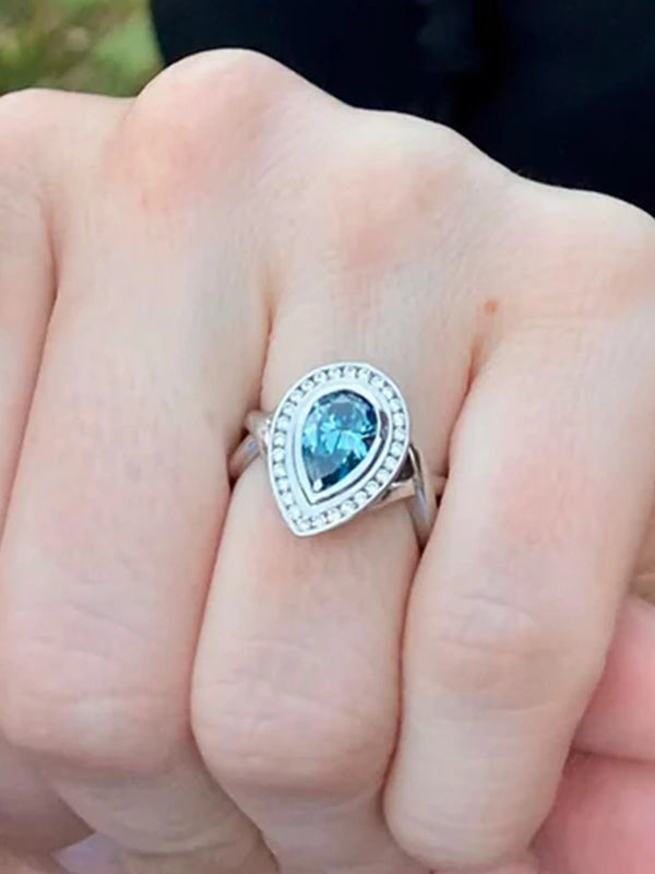 Ring with a blue gemstone on a finger against a blurred natural background