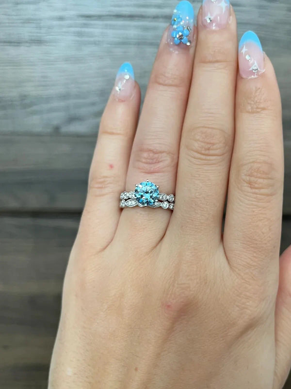 Hand wearing a silver ring with blue gemstone against a wooden background