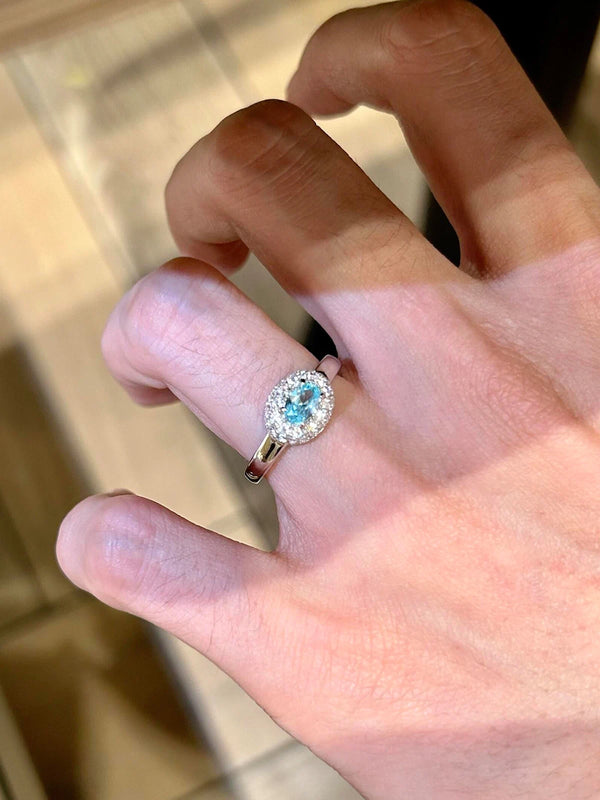 Hand wearing a ring with a blue gemstone on a neutral background