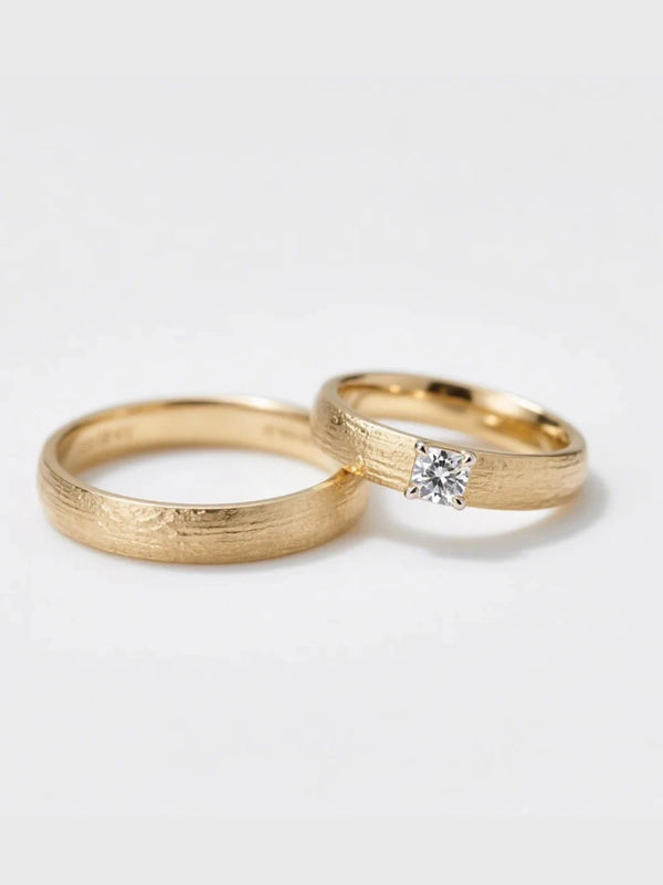 Two gold rings with one featuring a diamond on a light gray background