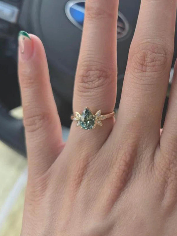 Hand wearing a ring with a green gemstone in front of a blurred car interior.