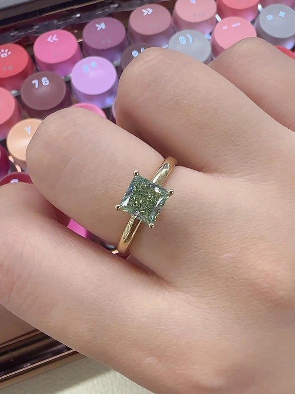 Gold ring with a green gemstone on a hand, with a colorful keyboard in the background.