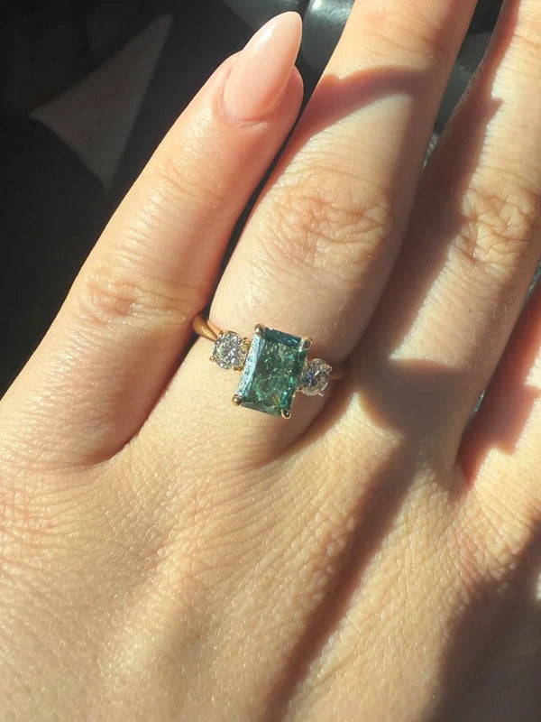 Close-up of a hand wearing a ring with a green gemstone on a dark background