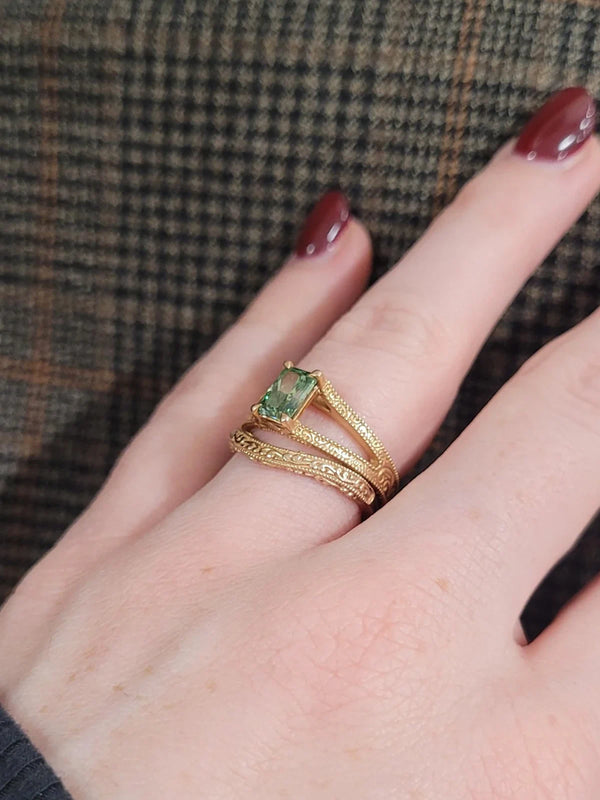 Gold ring with a green gemstone on a finger against a plaid fabric background