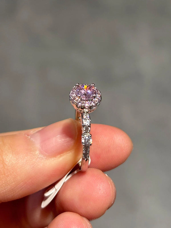 Ring with a purple gemstone held between fingers against a gray background
