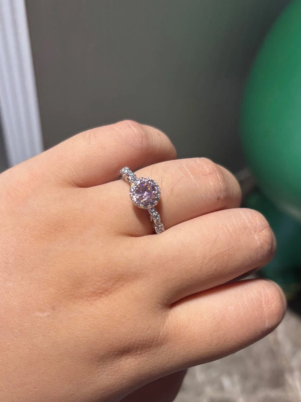 Hand wearing a ring with a pink gemstone on a blurred background