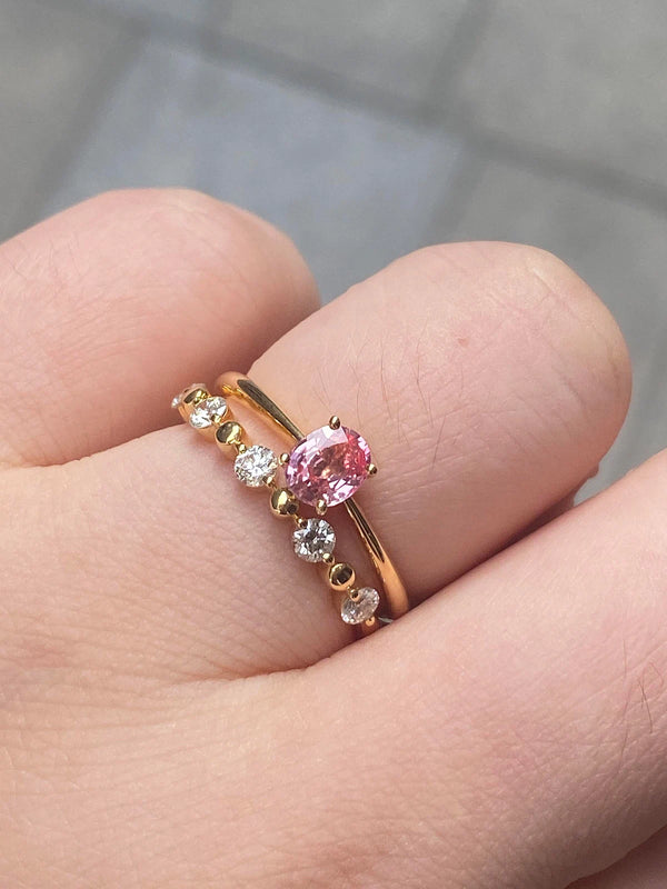 Gold ring with a pink gemstone on a finger against a neutral background