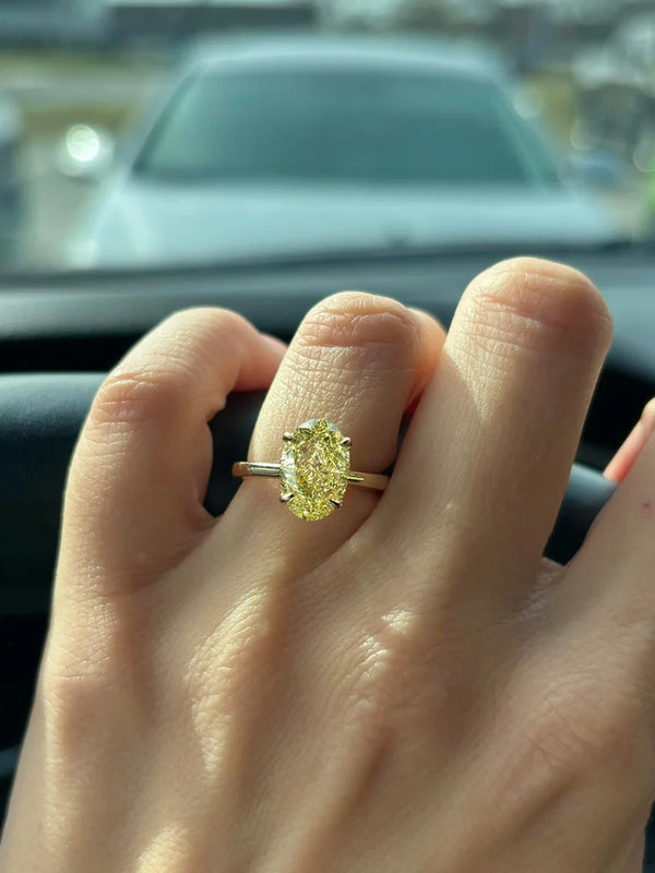 Hand wearing a yellow diamond ring with a blurred background