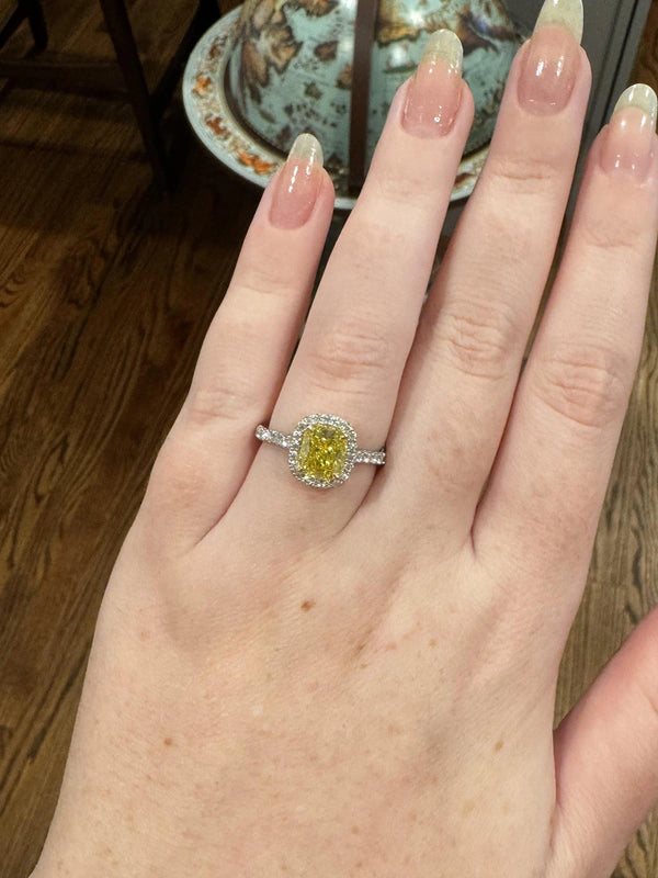 Hand wearing a ring with a yellow gemstone on a wooden floor.