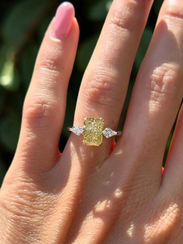 Yellow diamond ring with two smaller diamonds on a hand against a blurred natural background